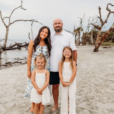 Family posing on a beach with dead trees in the background.
