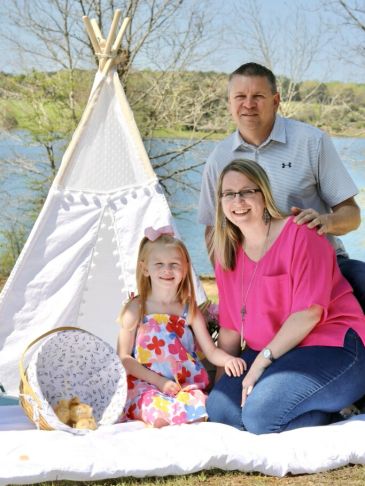 Family sitting outdoors by a teepee near water.