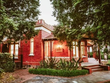 A charming red brick house surrounded by lush greenery and trees.
