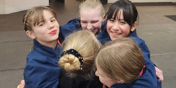 A group of five girls joyfully hugging each other indoors.