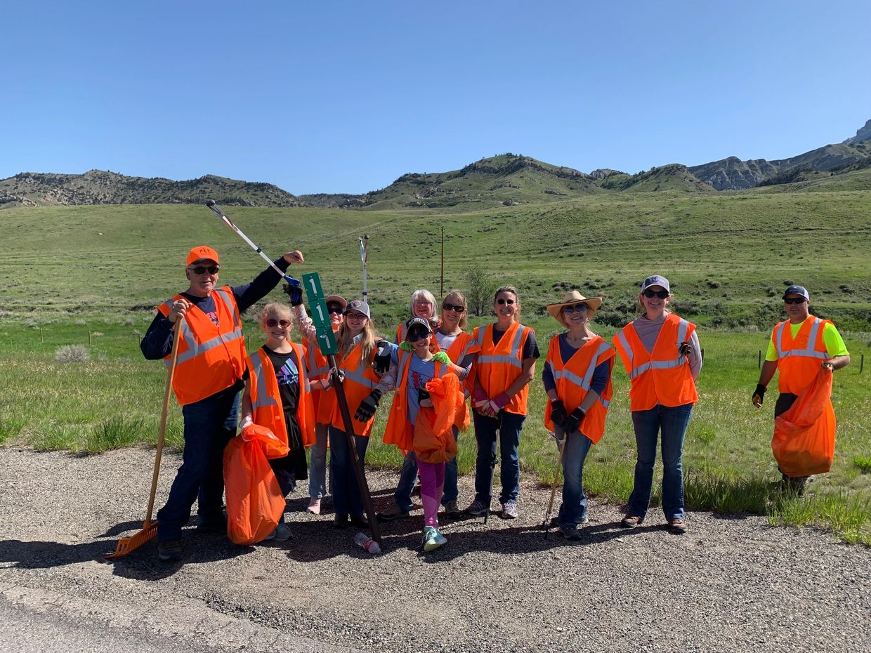 Group wearing orange safety vests outdoors with tools and bags.