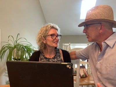 A man and woman engaged in a conversation indoors, with a laptop and plants nearby.