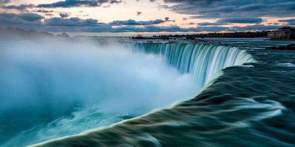 View of Niagara Falls at sunset with mist and flowing water.