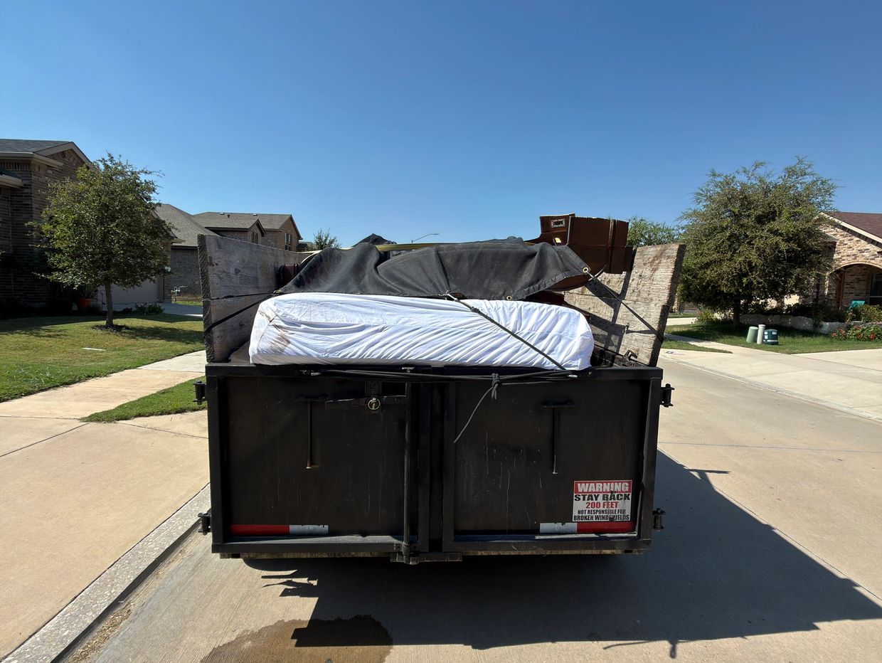 A trailer loaded with household items, including a mattress, parked in a suburban neighborhood.