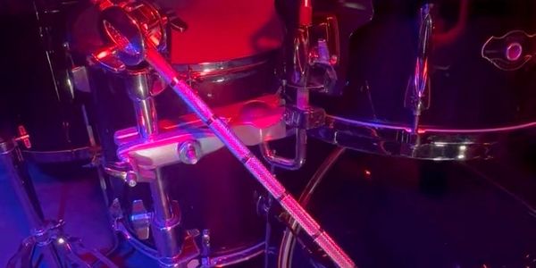 Close-up of drum set hardware under purple red lighting.