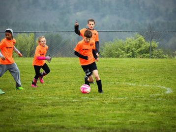 Kids playing soccer outdoors in orange jerseys.