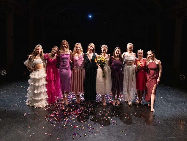 A group of women in elegant dresses posing on stage with confetti.