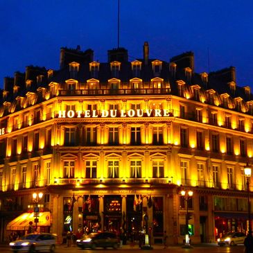 The illuminated Hotel du Louvre building at night in Paris.