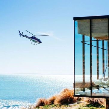 Helicopter flying near a modern glass house overlooking the ocean.