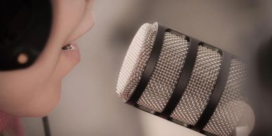Close-up of a person speaking into a microphone with headphones on.