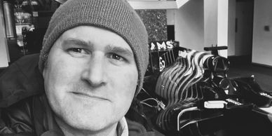 Man in a beanie taking a selfie indoors with clothes hangers in the background.