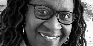 Close-up black and white portrait of a smiling woman with glasses and dreadlocks.