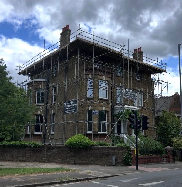 Old brick house with scaffolding under cloudy sky.