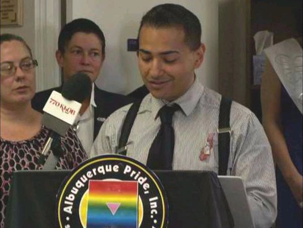 Man speaking at Albuquerque Pride event with microphone and audience.