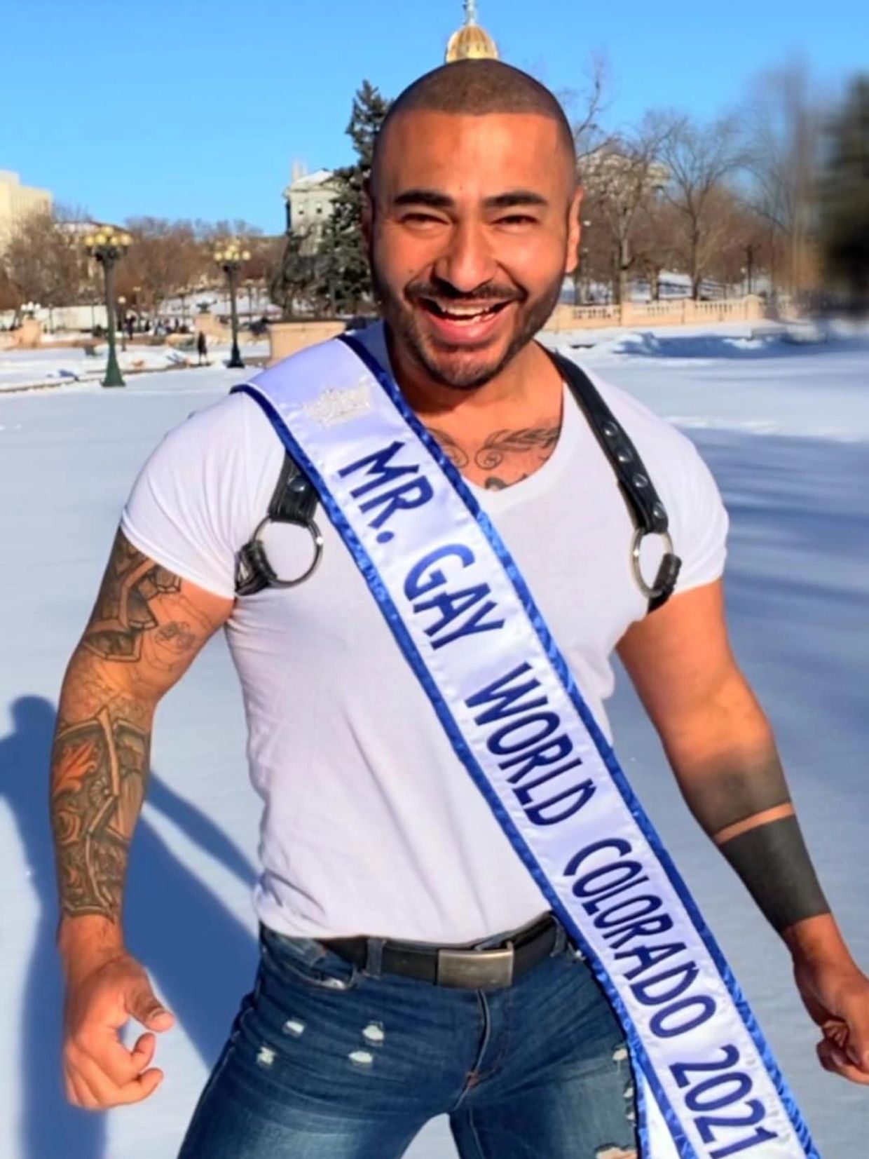 Smiling man wearing a Mr. Gay World Colorado 2021 sash outdoors in winter.
