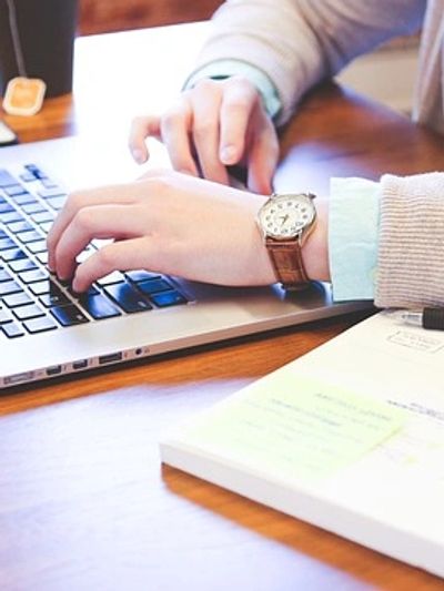 A person performing Christian book editing on a laptop with a coffee cup in the background. 