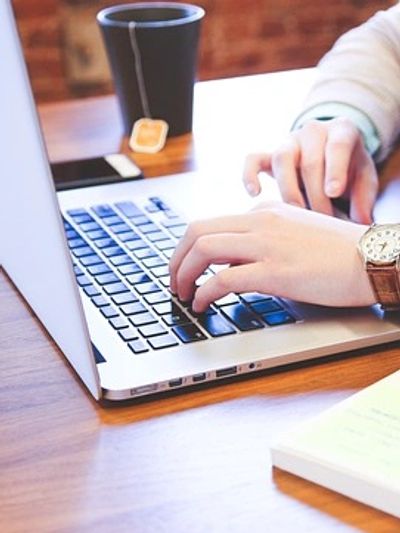 A person performing Christian book editing on a laptop with a coffee cup in the background. 