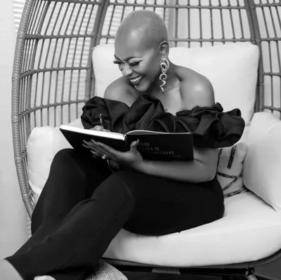 Woman in black outfit joyfully reading a book while seated in a cozy chair.