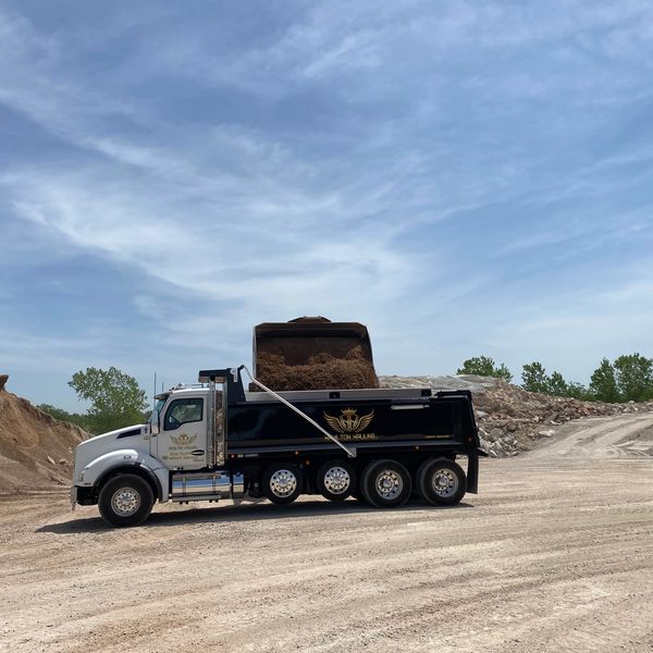A dump truck being loaded with dirt at a construction site under a blue sky.