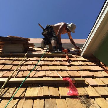 Man working shirtless on a roof under clear blue sky.
