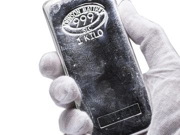 Hand holding a 1-kilo silver bar stamped 999 purity.
