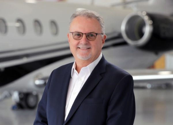 Smiling businessman in glasses stands in front of a private jet.