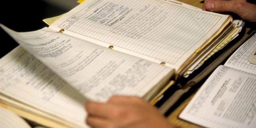 Hands flipping through detailed handwritten records in a binder.