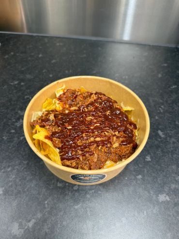 A bowl of nachos topped with chili and sauce.