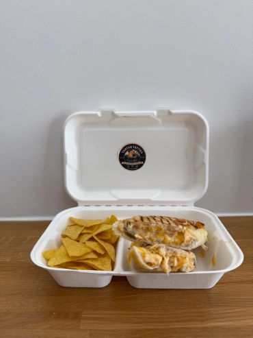 Takeout container with grilled chicken sandwich and tortilla chips.