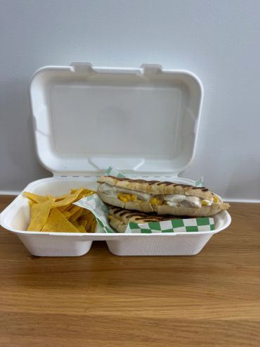 Grilled sandwich with chips in a takeout container.