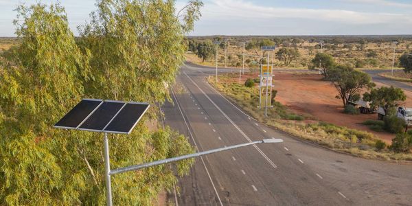 Solar-powered streetlights line a rural road in a dry landscape.