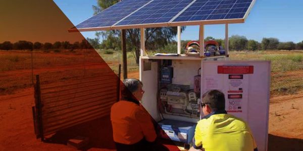Two people inspecting a solar-powered electrical box in an outdoor rural setting.