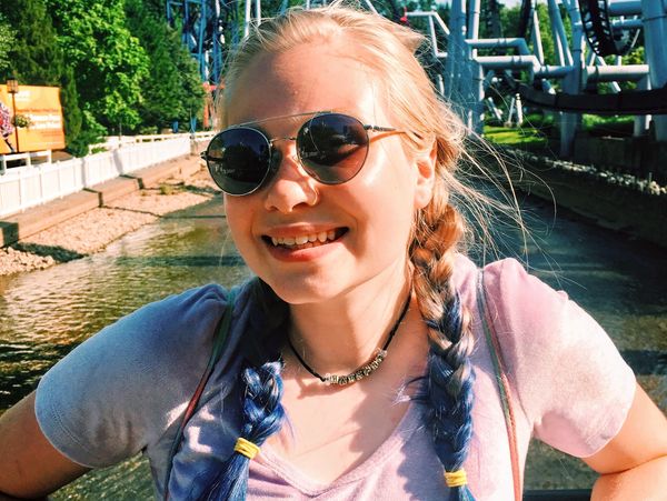 Felicia in front of creek and rollercoasters in sunglasses and braids