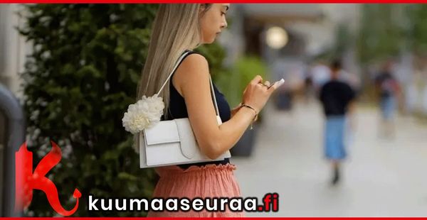 A woman with a white handbag and a flower accessory checks her phone outdoors.