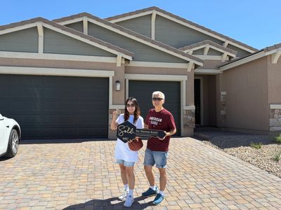 Happy couple holding a sold sign in front of their new house on a sunny day.
