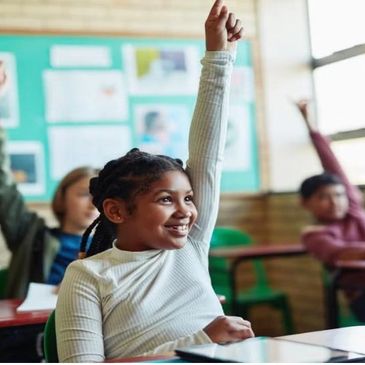 A smiling student eagerly raises her hand in class.