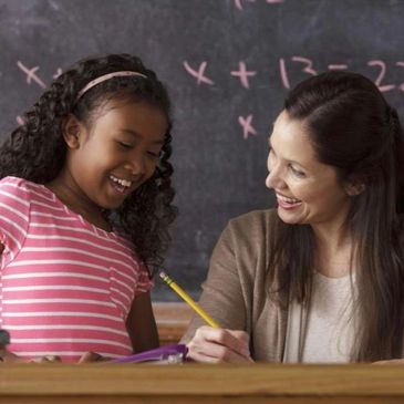 Teacher helping a young girl with math homework in class.
