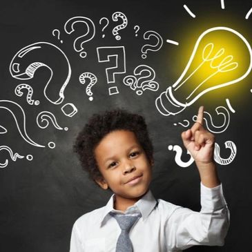 Young boy pointing at a glowing light bulb amidst question marks on chalkboard.