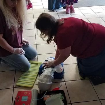 Two women practicing CPR on a mannequin with an AED nearby.