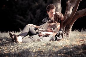 A young couple romantically reclining against a tree.