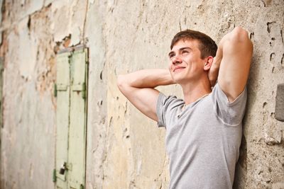A young man standing by a wall deep in thought.