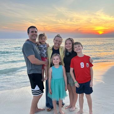 Family of six smiling on the beach during a vibrant sunset.