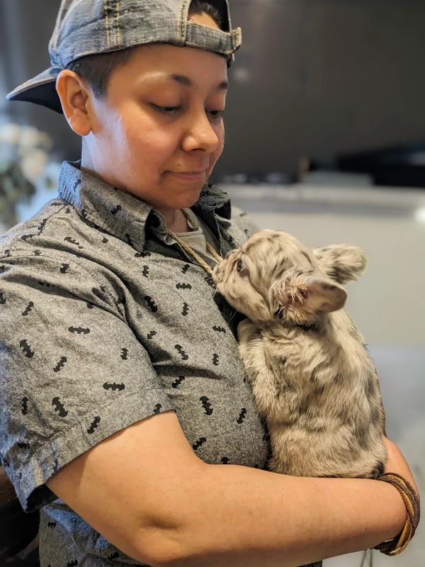 An Aztec woman holding a small Frenchie puppy.