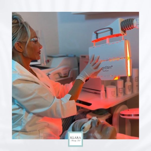 A technician uses a red light therapy device on a client's face in a skincare clinic.