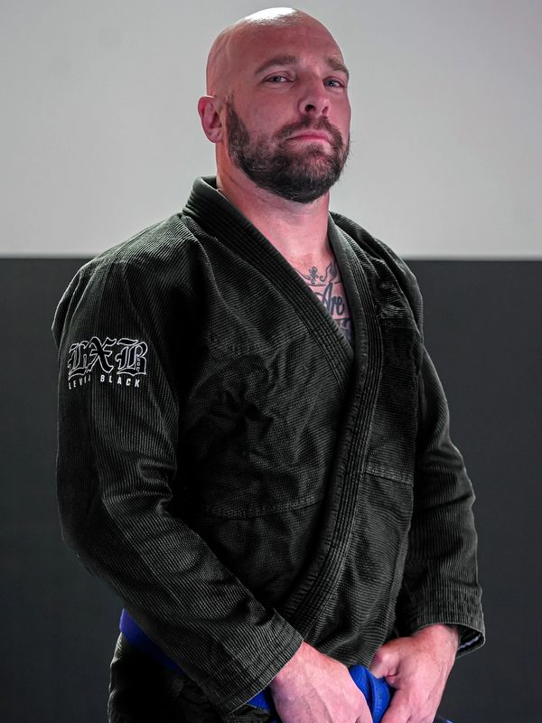 Bald man in black martial arts gi holding a blue belt.