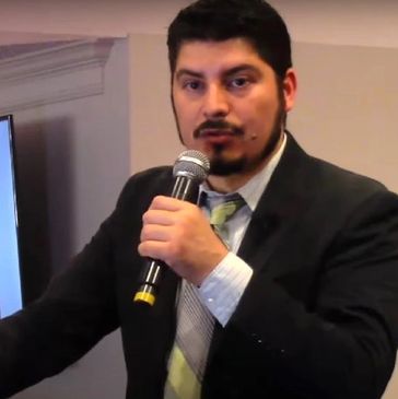 Angel Farías speaking with a wireless handheld microphone.