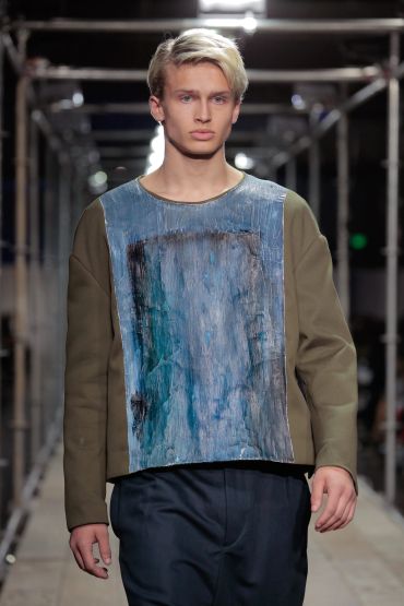 Male model in a blue and brown textured outfit on runway.
