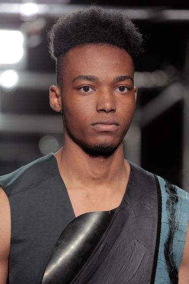Close-up of a man with textured hair and a serious expression in a fashion setting.