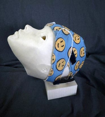 A white mannequin head wearing a blue strap with smiley faces on a black background.