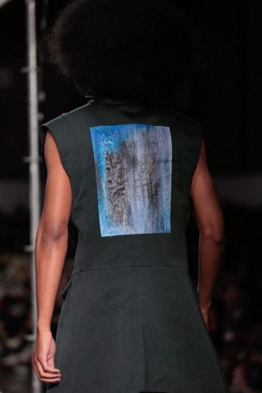 Model wearing a sleeveless black top with an abstract blue and gray artwork on the back.